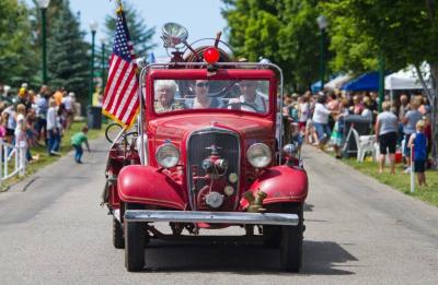 A man riding in a red truck with two women in the parade